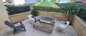 Une terrasse avec une table et des chaises en bois, un parasol vert et un mur en briques.