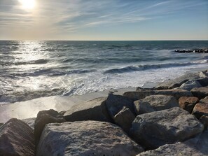 Un rivage rocheux battu par les vagues, un ciel dégagé et un soleil éclatant.