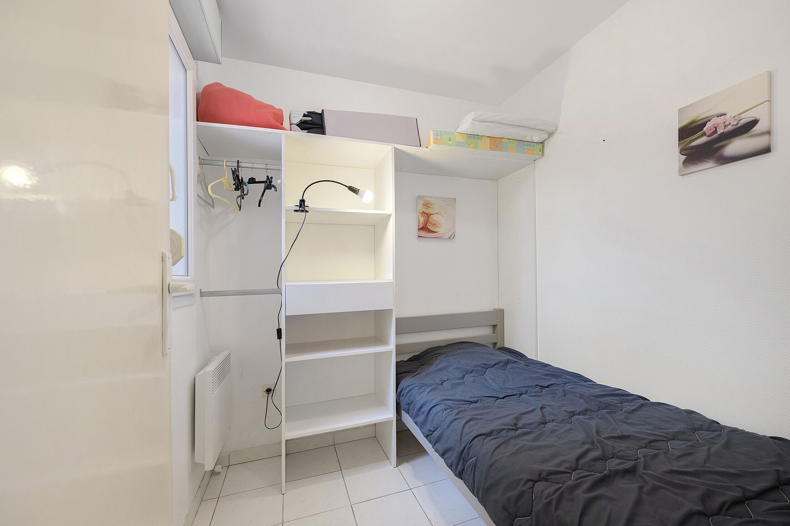 Een kleine, compacte kamer met een stapelbed, een witte kast en een radiator.