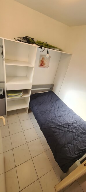 A compact room with a bed, a white wardrobe, and a small desk.