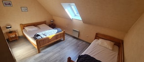 Une chambre avec un plafond en pente, un puits de lumiĂšre, un lit, une table de chevet et un radiateur.