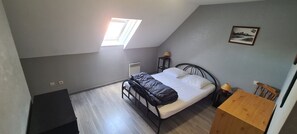 Une chambre Ă coucher avec un lit, une petite table, une chaise, une fenĂȘtre et un tableau au mur.