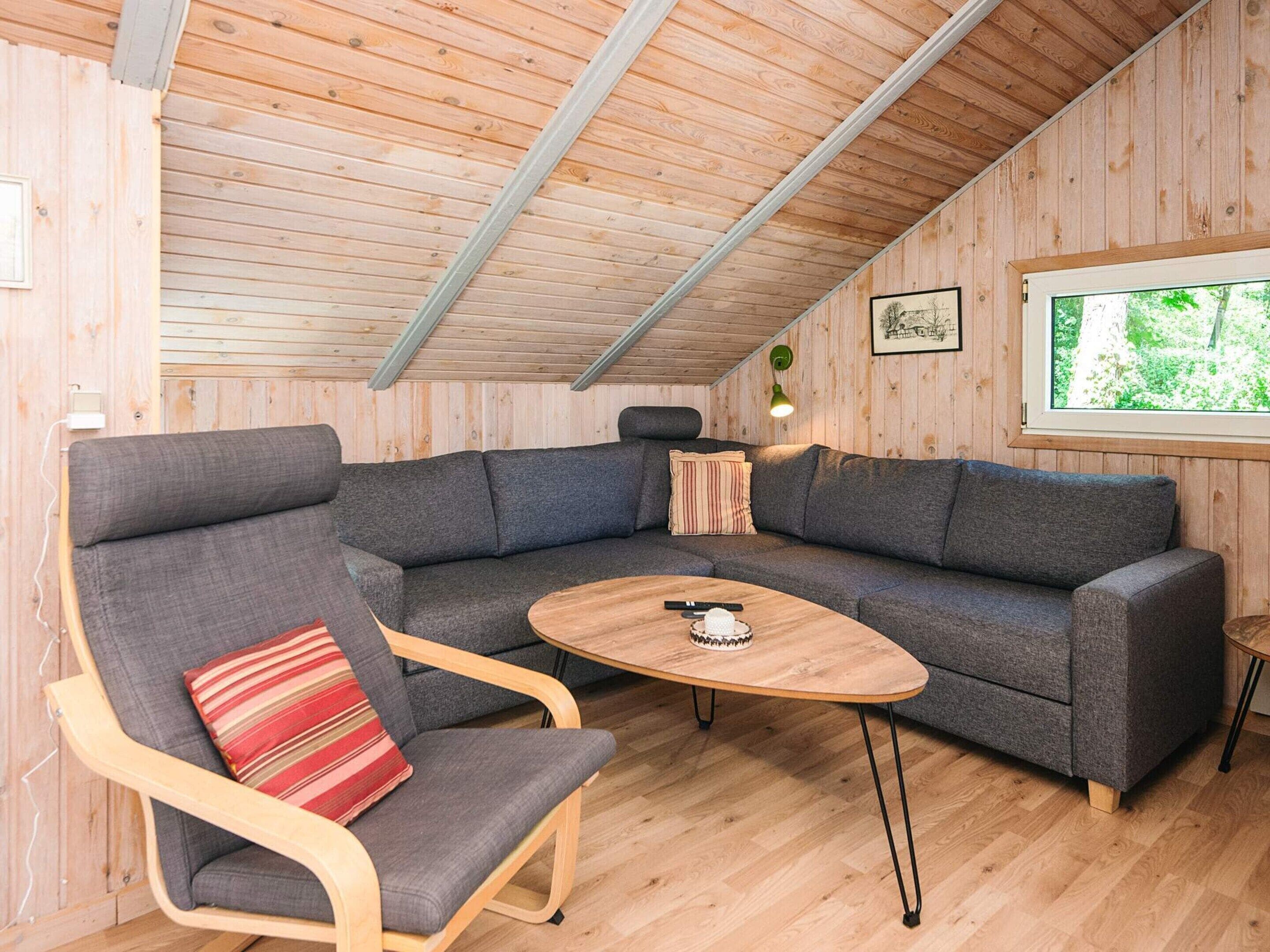 A cozy room with a wooden ceiling, a gray sectional sofa, a wooden coffee table, and a chair with a striped pillow.