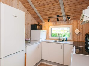 Eine kleine Küche mit weißen Schränken, einem Kühlschrank, einer Mikrowelle und einem Fenster mit Blick auf Grünflächen.