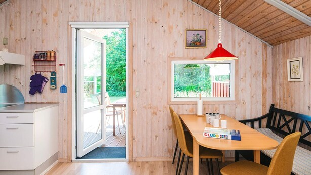 A wooden interior with a dining table, chairs, a kitchen area, and a window with a view of greenery. - 4 Star Holiday Home in Hovborg (Hovborg)