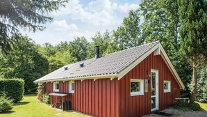 A red wooden cabin with a sloped roof, a small porch, and a gravel driveway. - 4 Star Holiday Home in Hovborg (Hovborg)