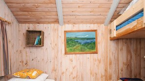 A wooden room with bunk beds, a framed landscape painting, a shelf with books, and a bed with a pillow and a book. - 4 Star Holiday Home in Hovborg (Hovborg)