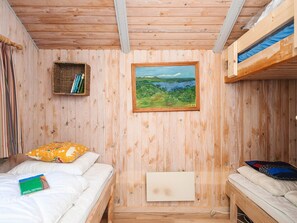 A wooden room with bunk beds, a framed landscape painting, a shelf with books, and a bed with a pillow and a book. - 4 Star Holiday Home in Hovborg (Hovborg)