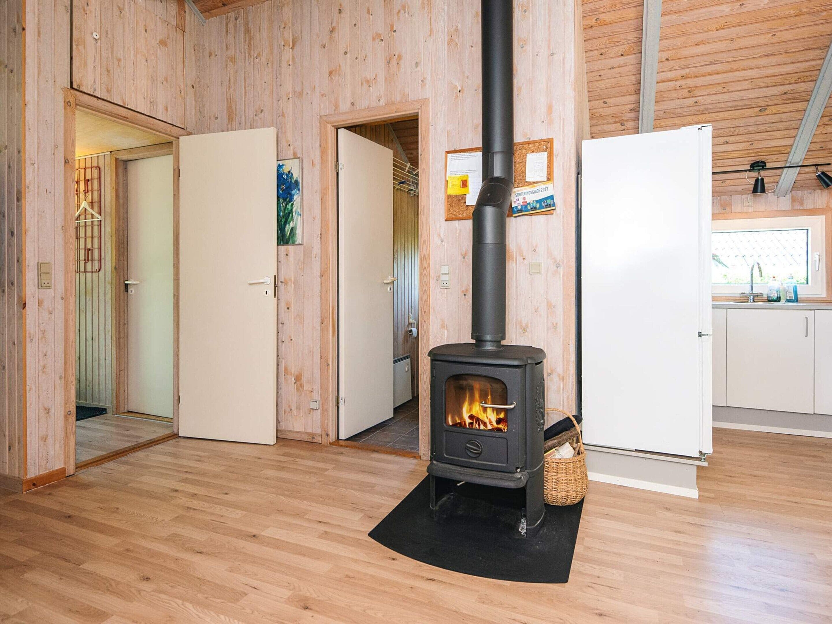 Ein Holzinnenraum mit einem zentralen Holzofen, einem weißen Kühlschrank und einer Küchenzeile mit Fenster.