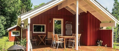 A red wooden cabin with a covered porch, a table, and chairs.