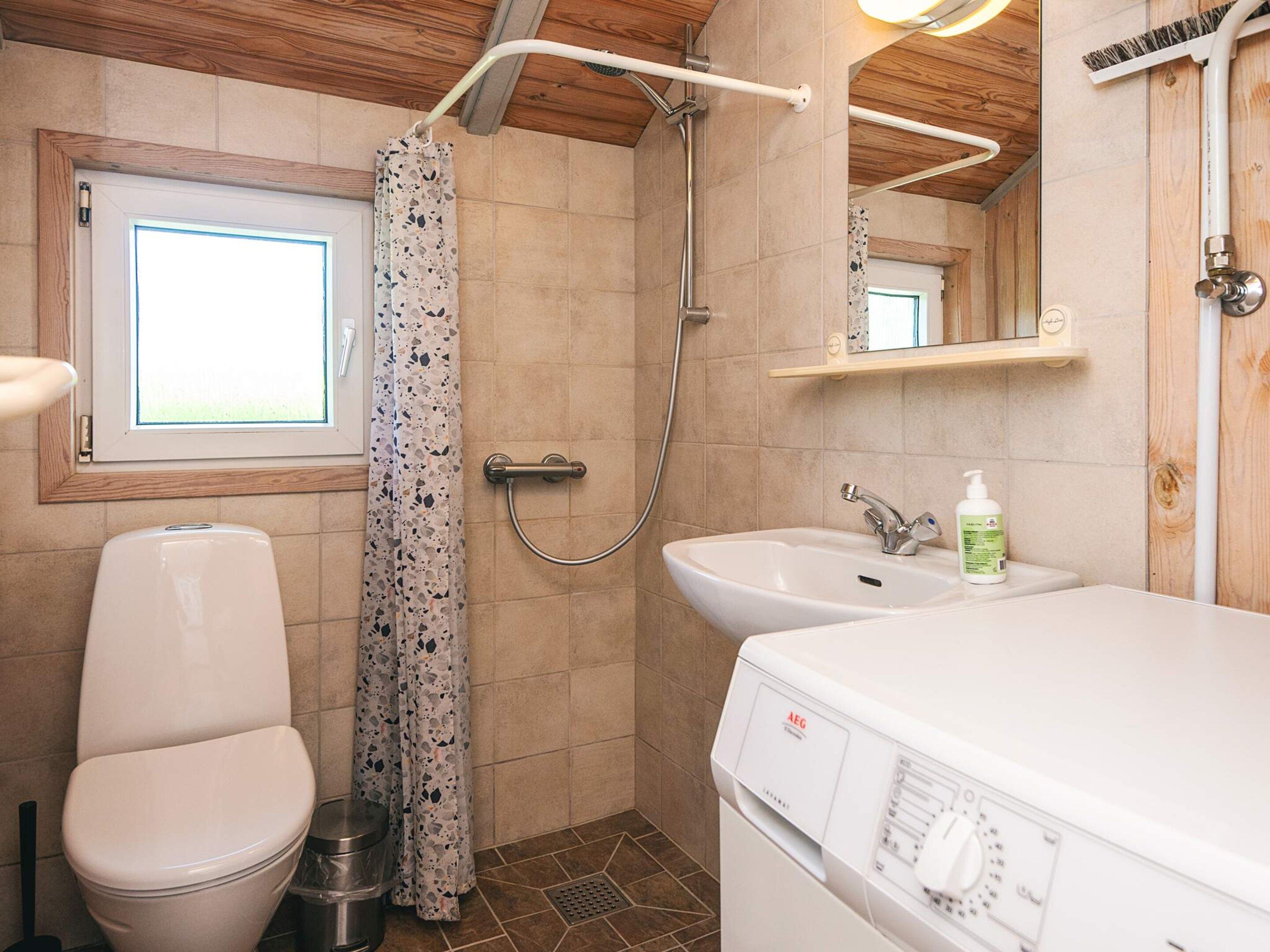 A bathroom with a toilet, shower, sink, and a window.