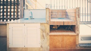 A small outdoor kitchen with a sink, a built-in grill, and a window overlooking the street.