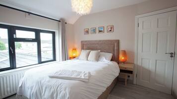 A bedroom with a large bed, two bedside lamps, a window with a view, and a door.