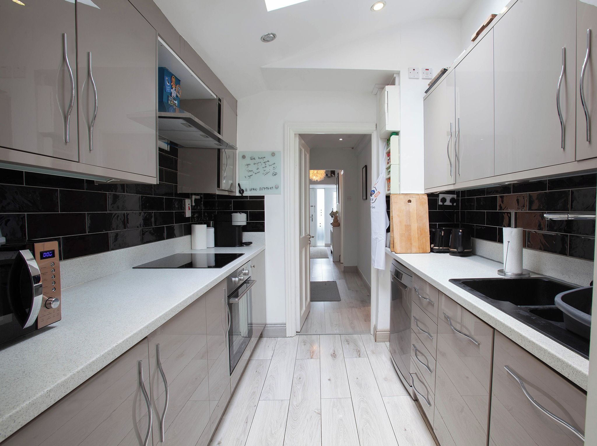 A modern kitchen with stainless steel appliances, black and white tiled backsplash, and a wooden floor.