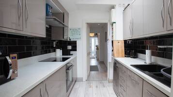 A modern kitchen with stainless steel appliances, black and white tiled backsplash, and a wooden floor.