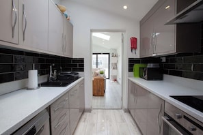 A modern kitchen with a central island, stainless steel appliances, and black tiled backsplash. - Modern 3BDR Home w Garden (Dublin)
