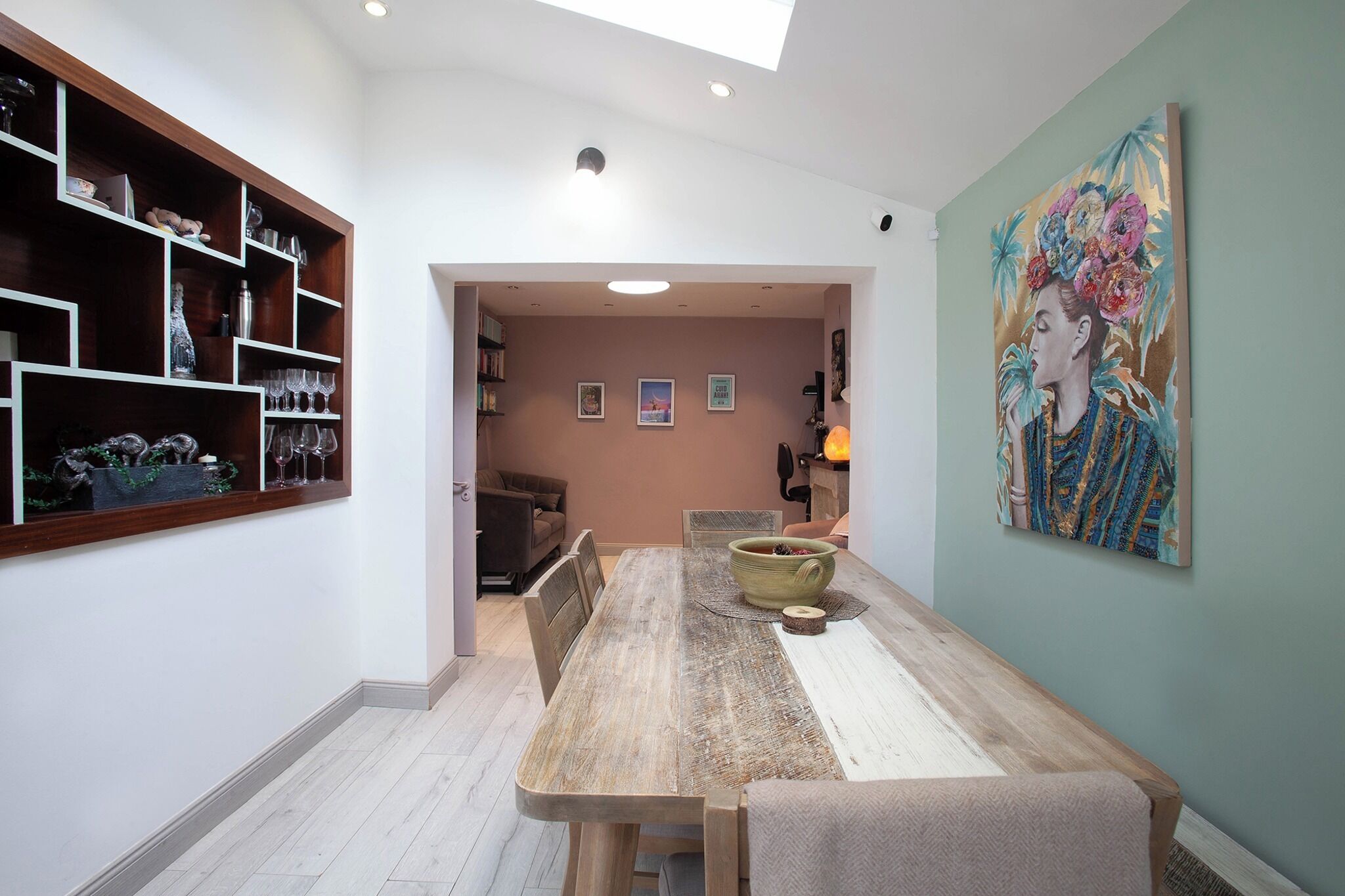 A dining area with a wooden table, chairs, a vase, and a painting on the wall.