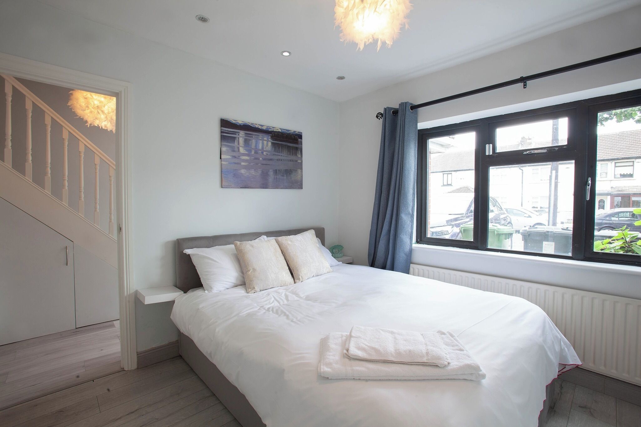 A bedroom with a bed, a painting, a window with curtains, and a staircase.