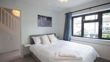 A bedroom with a bed, a painting, a window with curtains, and a staircase.