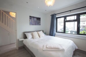 A bedroom with a bed, a painting, a window with curtains, and a staircase. - Modern 3BDR Home w Garden (Dublin)