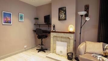 A living room with a fireplace, a sofa, a desk with a computer, and artwork on the walls.