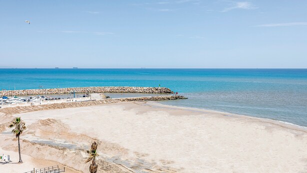 A beach with a rocky breakwater, clear blue water, and a sandy shore.