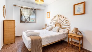 A bedroom with a bed, a bedside table, a lamp, a window with curtains, a picture on the wall, and a wardrobe.