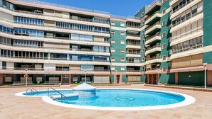 A multi-story hotel with a central swimming pool, balconies on each floor, and a clear sky.