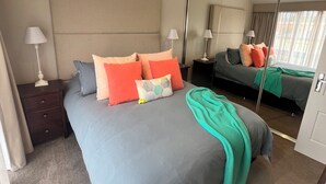 Ein Schlafzimmer mit Bett, Nachttischen, Deckenventilator, großem Spiegel und Blick nach draußen.