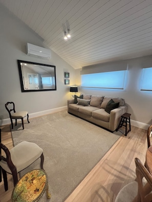 A living room with a sofa, chairs, a lamp, a mirror, and a window. - Seascape Cottage (Glenelg)