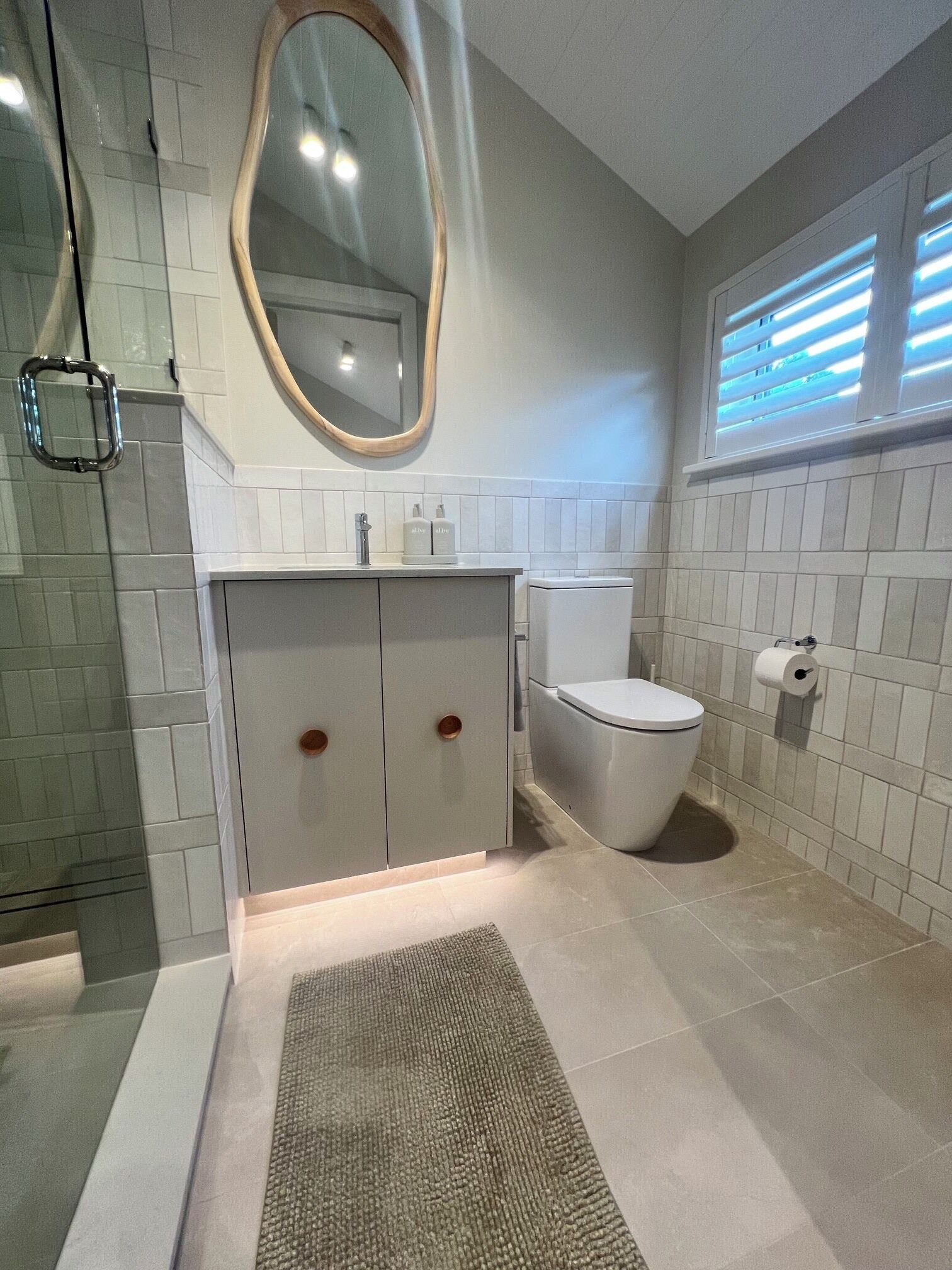 A bathroom with a toilet, a sink with a mirror, and a shower area.