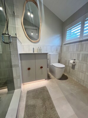 A bathroom with a toilet, a sink with a mirror, and a shower area. - Seascape Cottage (Glenelg)