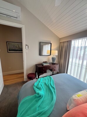 A hotel room with a bed, a desk, a chair, a mirror, a lamp, and a window with curtains. - Seascape Cottage (Glenelg)