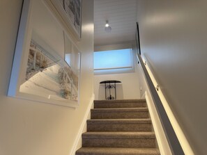 A carpeted staircase with a handrail, a skylight, and framed artwork on the walls. - Seascape Cottage (Glenelg)
