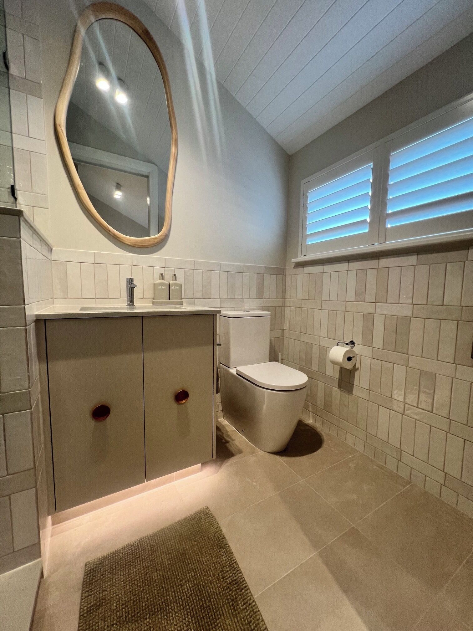 A bathroom with a toilet, a sink with a mirror, and a window with blinds.