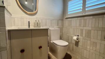 A bathroom with a toilet, a sink with a mirror, and a window with blinds.