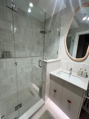 A modern bathroom with a glass-enclosed shower, a white sink with a mirror, and a tiled wall. - Seascape Cottage (Glenelg)