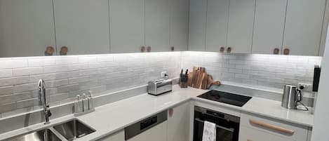A modern kitchen with white cabinetry, a built-in oven, a sink, and a clock on the wall.