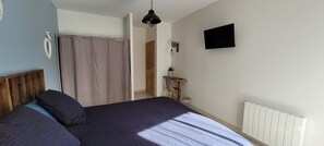 A bedroom with a bed, a shower curtain, a wooden headboard, a wall-mounted TV, and a radiator.
