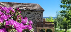 A stone building with a tiled roof, a wooden bench, and pink flowers in the foreground.