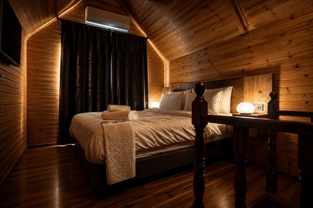 Una habitación acogedora de madera con una cama, una mesa con una lámpara y un equipo de aire acondicionado.