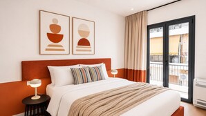 Una habitación de hotel moderna con una cama grande, dos mesitas de noche, un ventanal con cortinas y una obra de arte en la pared.