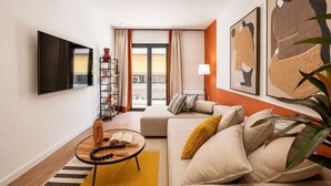 Una sala de estar con un sofá, una mesa de centro, una estantería y un televisor montado en la pared.