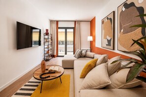 Ein Wohnzimmer mit einer Couch, einem Couchtisch, einem Bücherregal und einem an der Wand befestigten Fernseher.