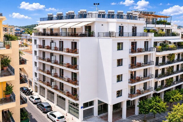 Ein mehrstöckiges Hotel mit Balkonen, einer Dachterrasse und einem Parkplatz.