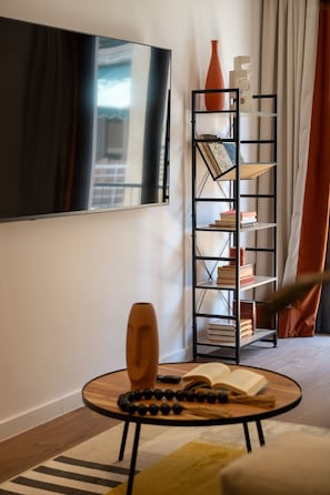 Ein modernes Wohnzimmer mit rundem Couchtisch, Bücherregal, einem großen Gemälde und einem Fenster mit Vorhängen.