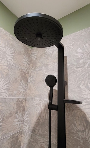Une pomme de douche au design circulaire, un flexible de douche et un levier de commande fixé au mur.