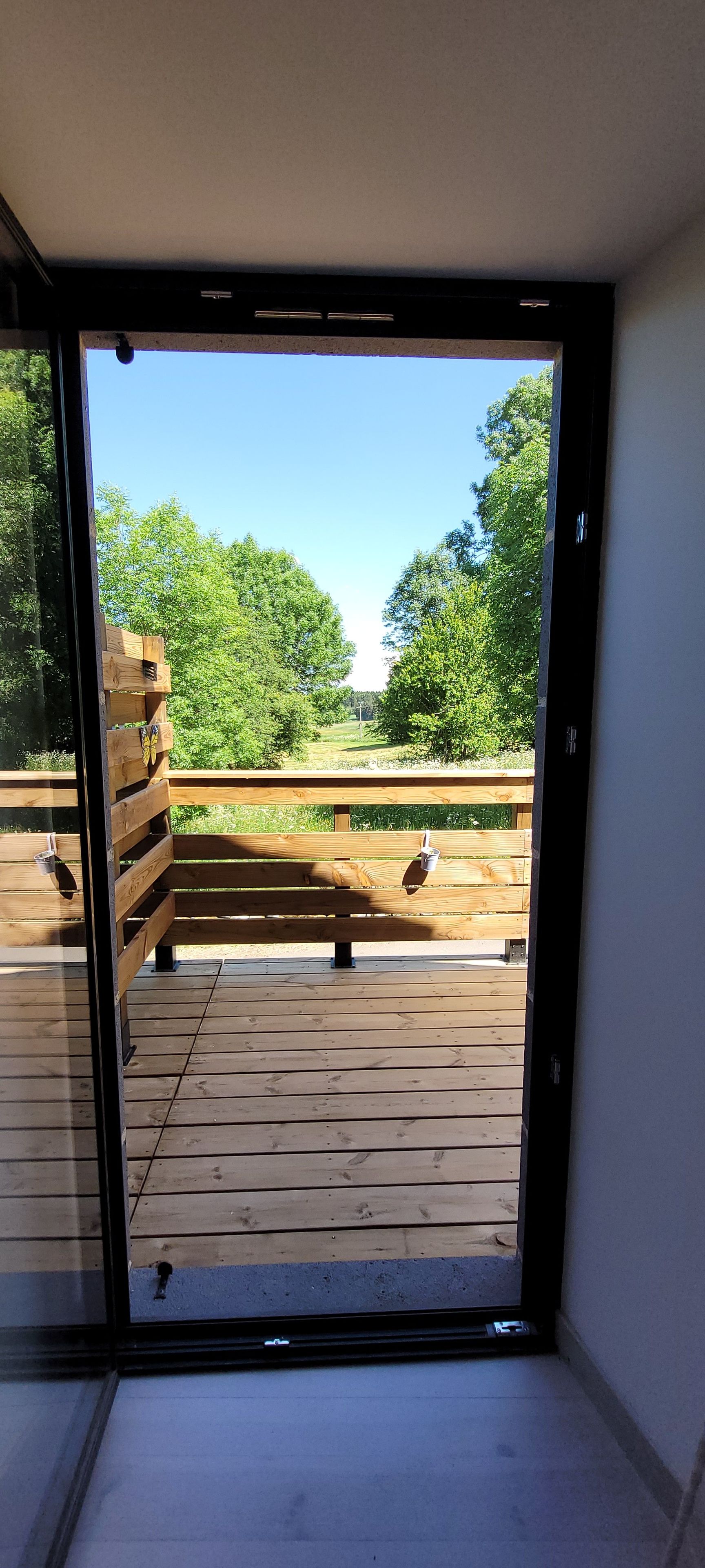 Uitzicht door een glazen deur op een houten terras met een bankje.