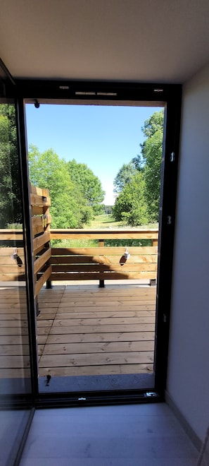 A view through a glass door to an outdoor wooden deck with a bench. - “Chambre Planèze” Guest Room with Private Terrace (Soulages)