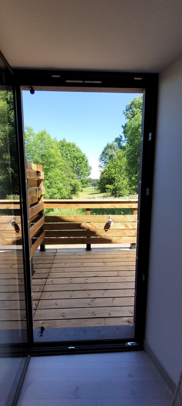 On aperçoit, à travers une porte vitrée, une terrasse en bois donnant sur l’extérieur, où se trouve un banc.